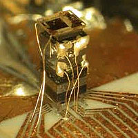 The 'physics package' of the chip-scale atomic clock includes (from the bottom) a laser, a lens, an optical attenuator to reduce the laser power, a waveplate that changes the polarization of the light, a cell containing a vapor of cesium atoms, and (on top) a photodiode to detect the laser light transmitted through the cell. The tiny gold wires provide electrical connections to the electronics for the clock.
<P>
NIST Photo