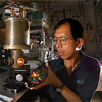 THE REAL HARRY POTTER? — A tungsten photonic lattice glows in a vacuum chamber as Sandia researcher Shawn Lin inspects an irridescent disk that contains approximately 1,000 tungsten photonic lattices. Most emissions from these filaments are in the near-infrared range, and may improve efficiencies of heat-driven engines like hybrid electric automobiles.
<P>(Photo by Randy Montoya) Courtesy Sandia National Labs.
