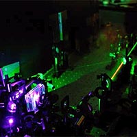 Photo depicts some of the apparatus used to make the three-photon state. At upper right (the black box peeking in from the edge of the frame) is the laser that produces 810nm photons (that's an infrared wavelength, but close enough to the visible part of the spectrum that you can still see it as the red beam in the photo). Most of the infrared beam is focused into a doubling crystal, inside the protective box at lower left, to produce violet photons. The violet photons are directed into the 'downconversion crystal', which is the brightest spot at lower left. Inside the downconversion crystal sometimes a violet photon will split in two, forming a pair of infrared photons, each with wavelength 810 nm. At the same time, a very small amount of the infrared beam is split off, to give a third photon. Outside the picture, these three photons are combined into a single beam of entangled photons in a state. 
<P>
Photo courtesy of University of Toronto.