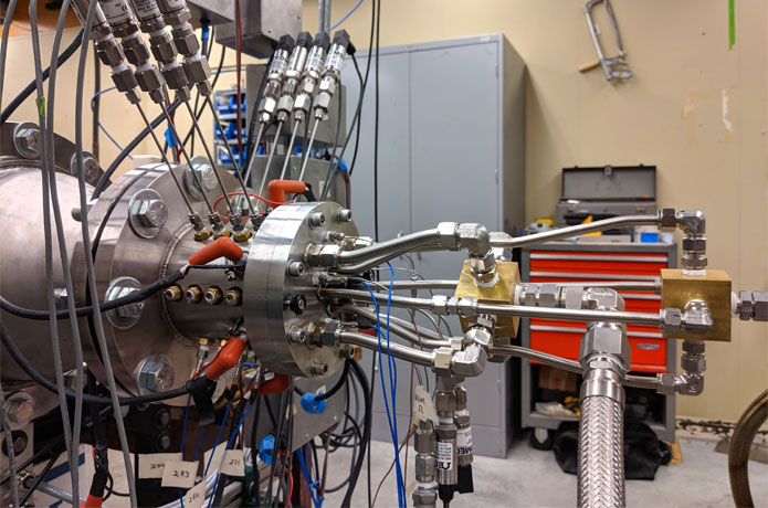 <p>The experimental rotating detonation engine</p>

<p>The researchers developed an experimental rotating detonation engine (shown here) where they could control different parameters, such as the size of the gap between the cylinders. The feed lines (right) direct the propellant flow into the engine. On the inside, there is another cylinder concentric to the outside piece. Sensors sticking out of the top of the engine (left) measure pressure along the length of the cylinder. The camera would be on the left-hand side, looking from the back end of the engine. James Koch/University of Washington</p>
